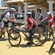 A man in biking gear talks to a group of young bikers on mountain bikes